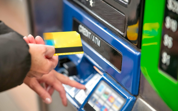 Une femme se tient devant un distributeur automatique avec sa carte bancaire