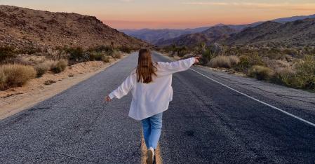 Une fille au pair court dans le désert, les bras grands ouverts, le long de l'autoroute.