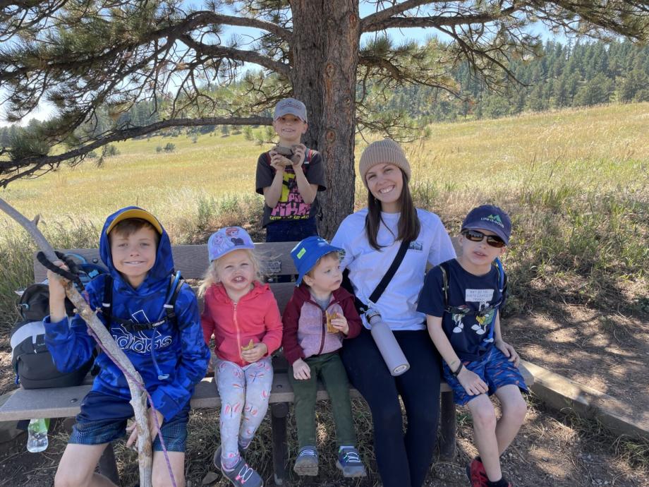 Une fille au pair assise dehors sur un banc avec cinq jeunes enfants