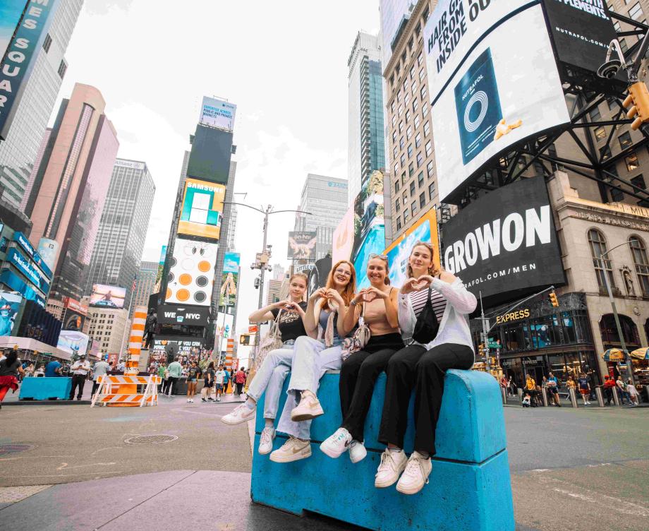 Un groupe de jeunes au pair assis côte à côte sur un bloc de béton à Times Square.