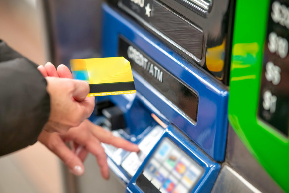 Une femme se tient devant un distributeur automatique avec sa carte bancaire