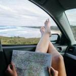 personne assise dans une voiture, tenant une carte routière, les pieds passés par la fenêtre